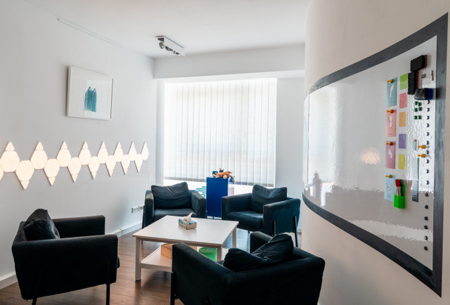 Sprechzimmer mit dunklen Sesseln um einen niedrigen Tisch und einer beschreibbaren Glaswand