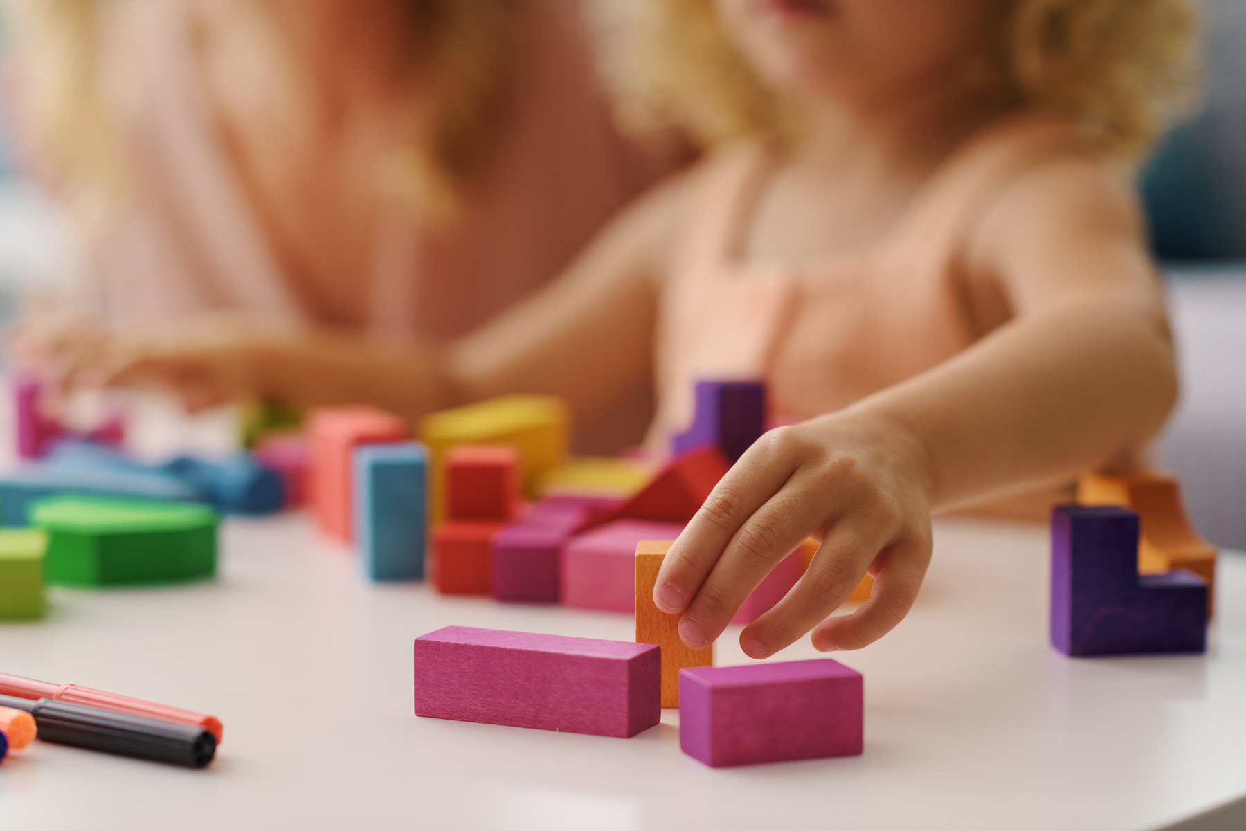 Kinderhand setzt einen bunten Holzbaustein auf einen Tisch
