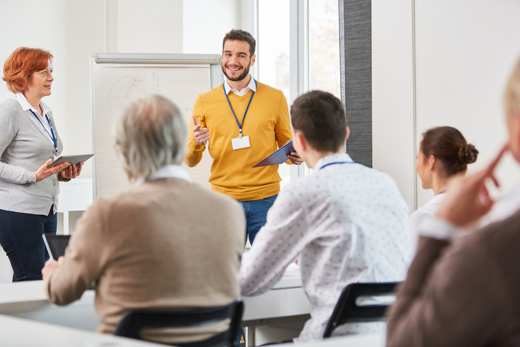 Dozent im Gespr&auml;ch mit einer Seminargruppe vor einem Flipchart