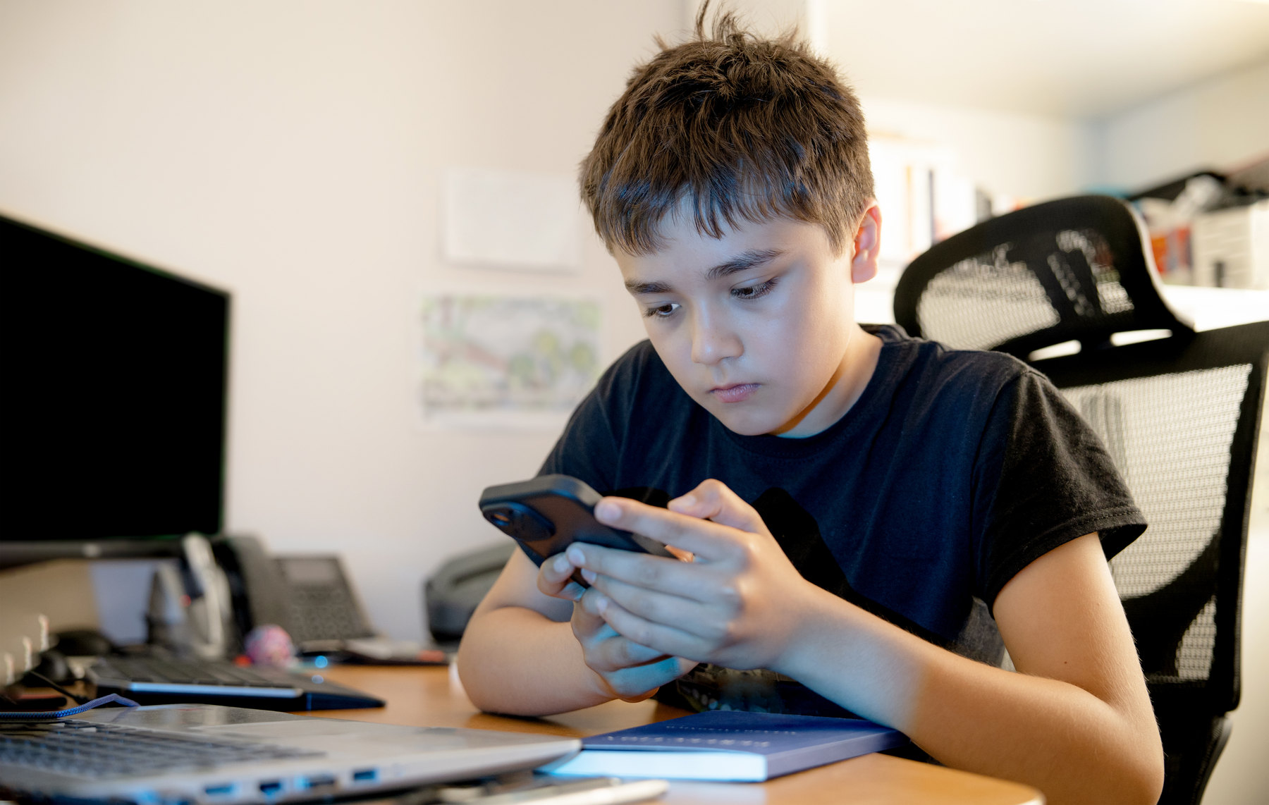 Junge sitzt am Schreibtisch und schaut auf sein Smartphone