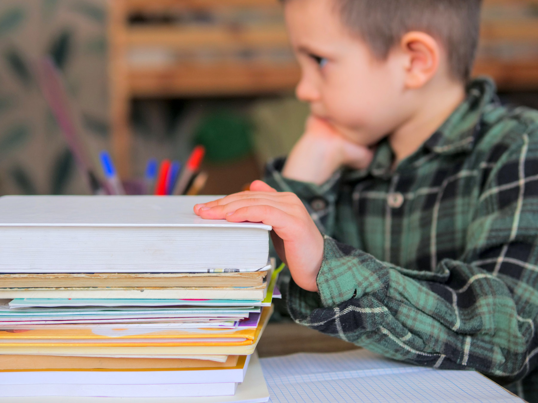 Junge sitzt am Schreibtisch und schaut an einem Stapel B&uuml;cher vorbei