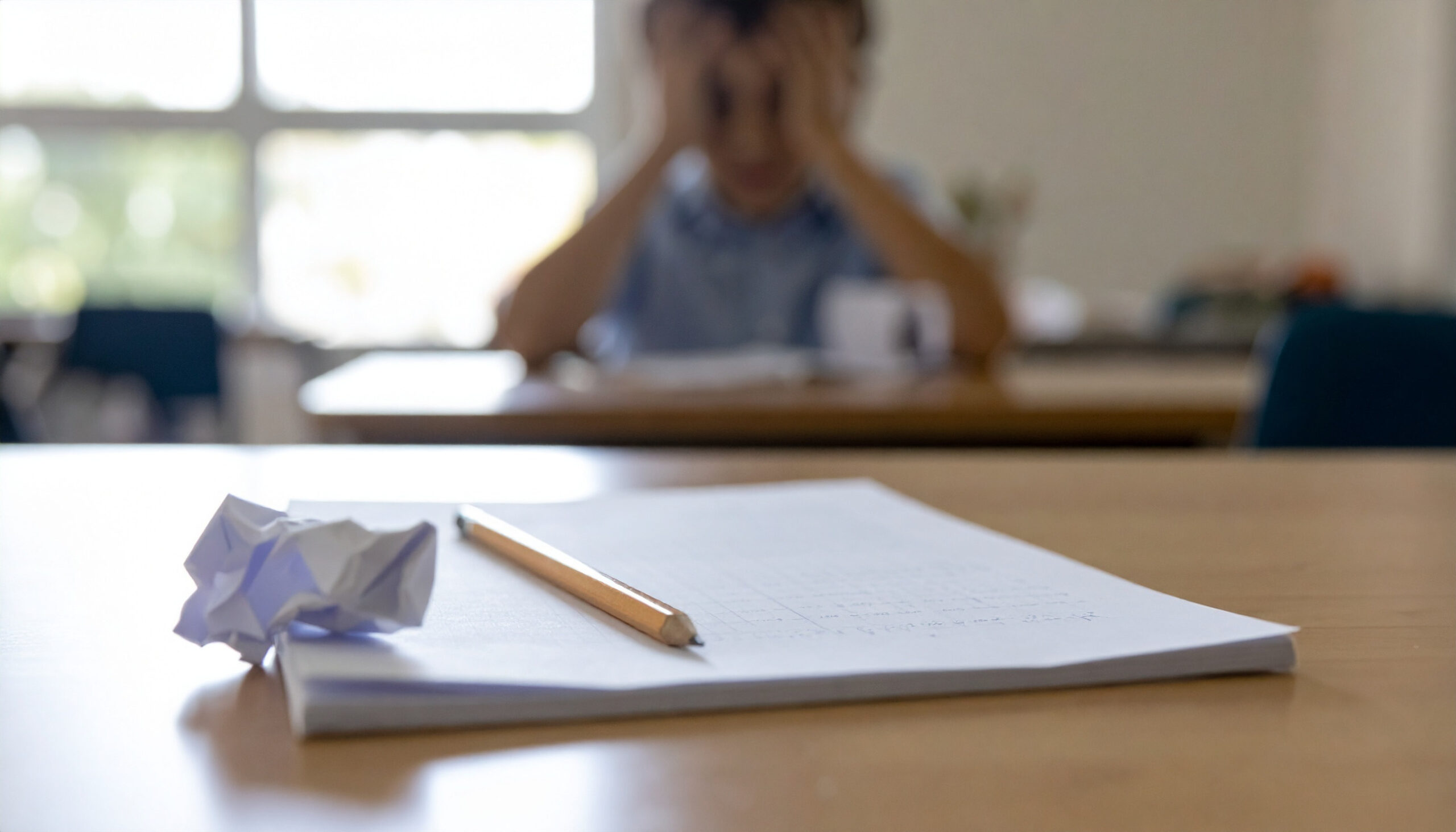 Kind sitzt mit dem Kopf in den H&auml;nden am Schreibtisch, davor ein zerkn&uuml;lltes Blatt